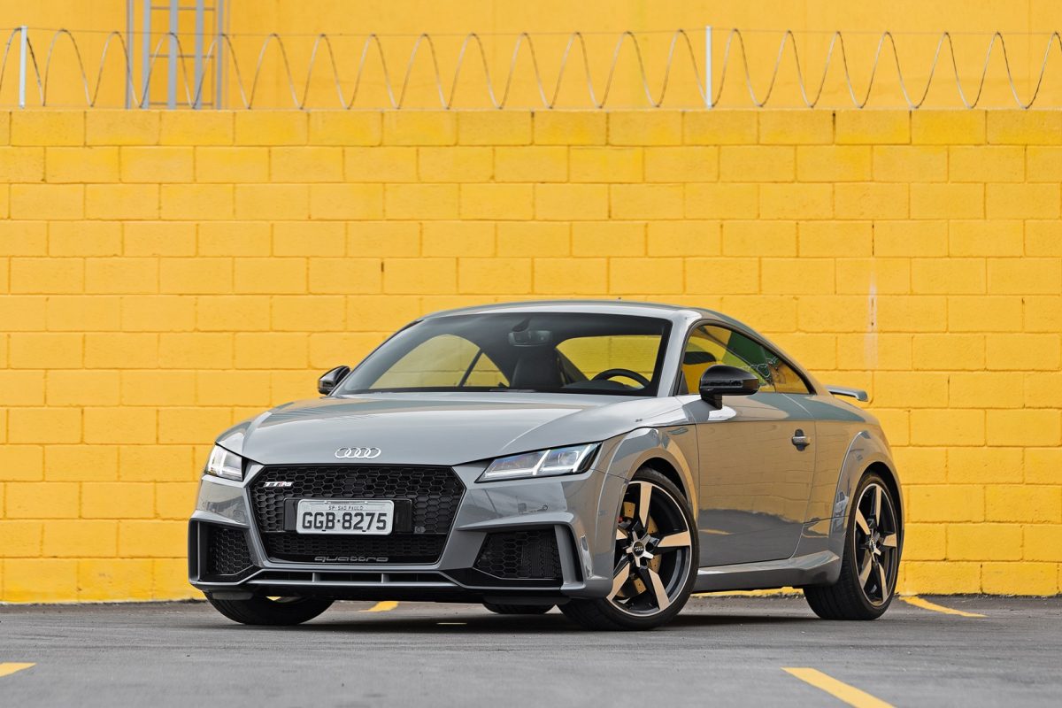 Audi TT RS cinza parado de frente com muro amarelo ao fundo