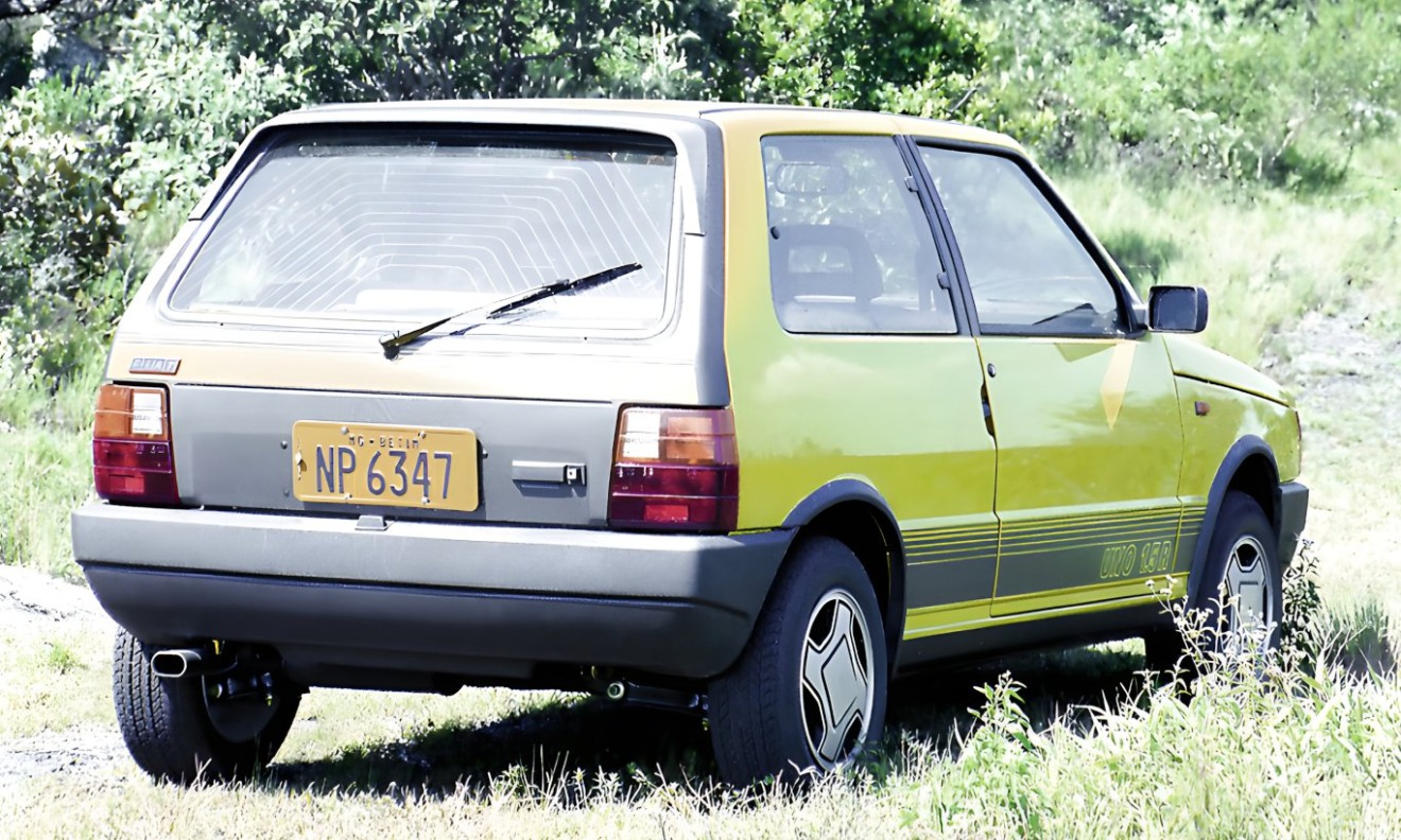 Fiat Uno 1.5R amarelo parado de traseira. O para-choque sem pintura é um item em desuso atualmente. 