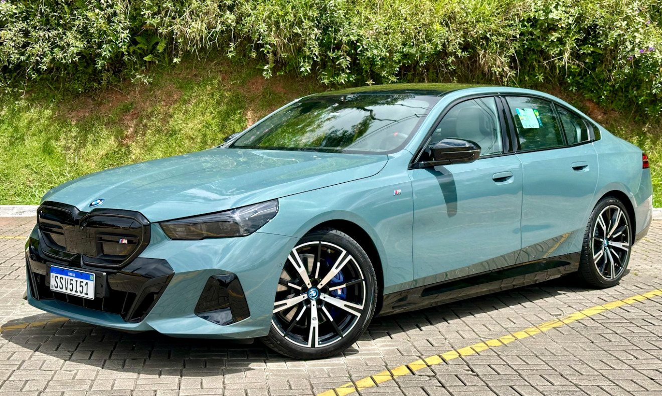 BMW i5 verde parado de dianteira com plantas ao fundo