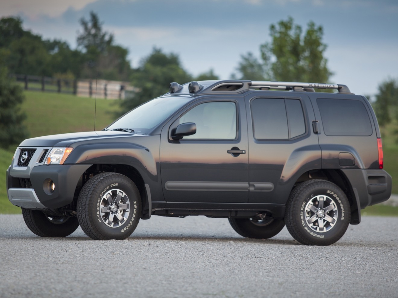 Nissan Xterra cinza parado de lado com as rodas dianteiras viradas e árvore ao fundo