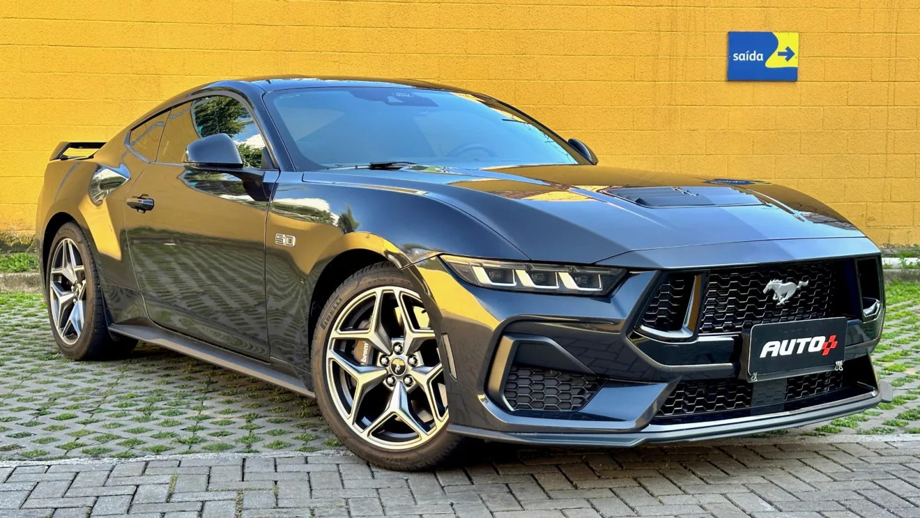 Ford Mustang GT cinza de frente em um muro amarelo. O nome tem uma relação inspiracional com o avião North American P-51 Mustang