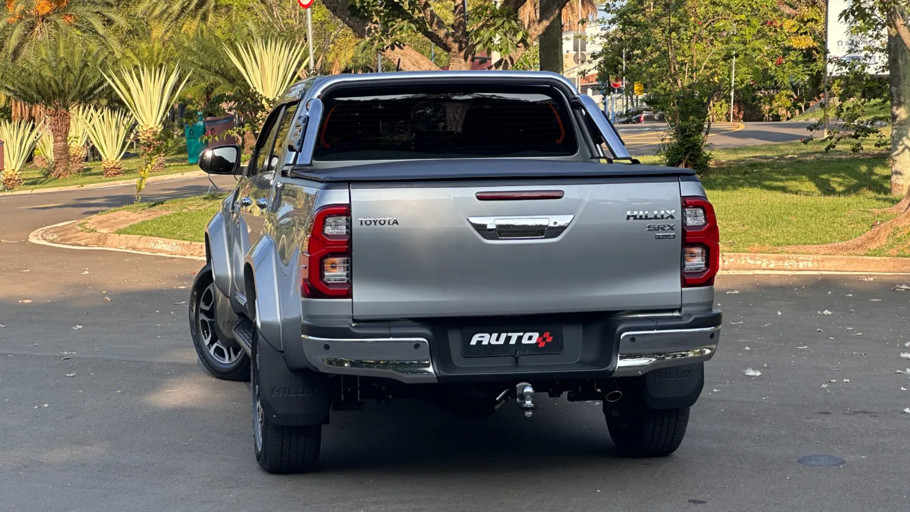 Caminhonete  Toyota Hilux SRX Plus prata parada de traseira com árvores ao fundo 