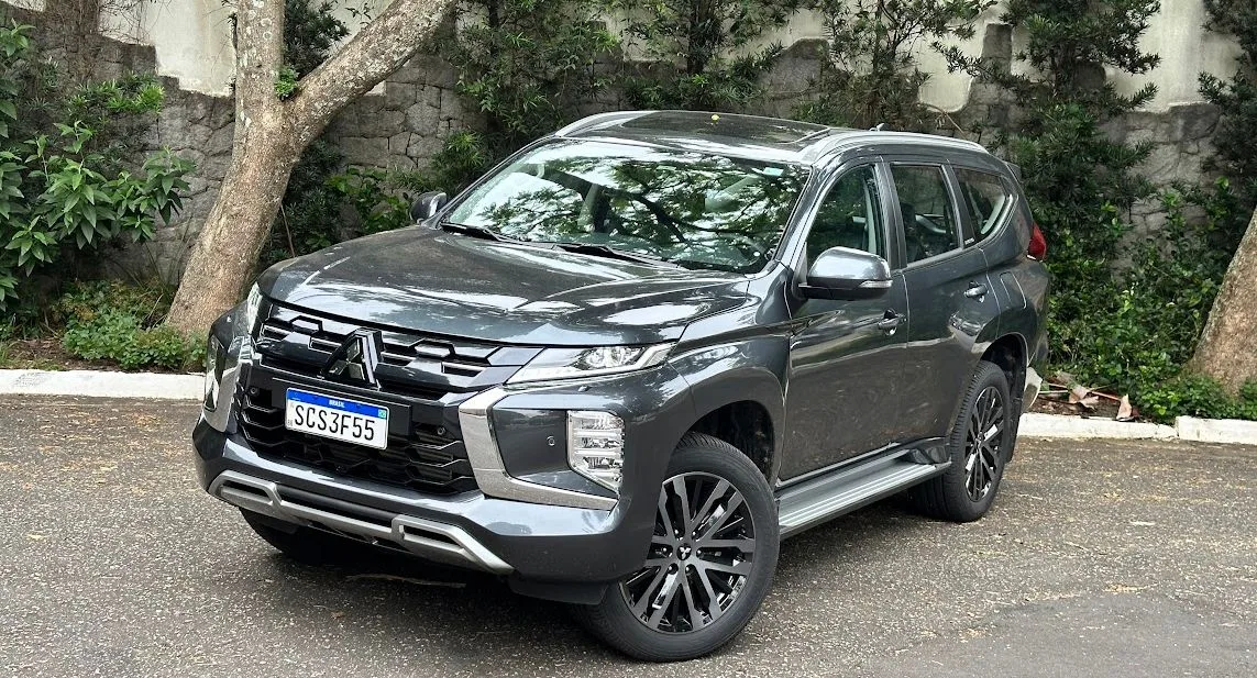Mitsubishi Pajero Sport cinza parado de frente com árvores ao fundo