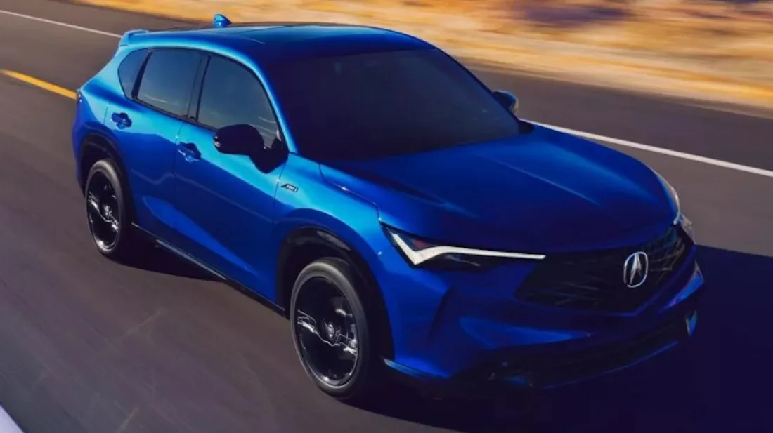 Acura ADX azul, visto de frente, com faróis acesos e andando em uma estrada