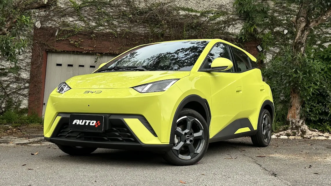 BYD Dolphin Mini amarelo parado em frente a um portão branco e com árvores ao fundo