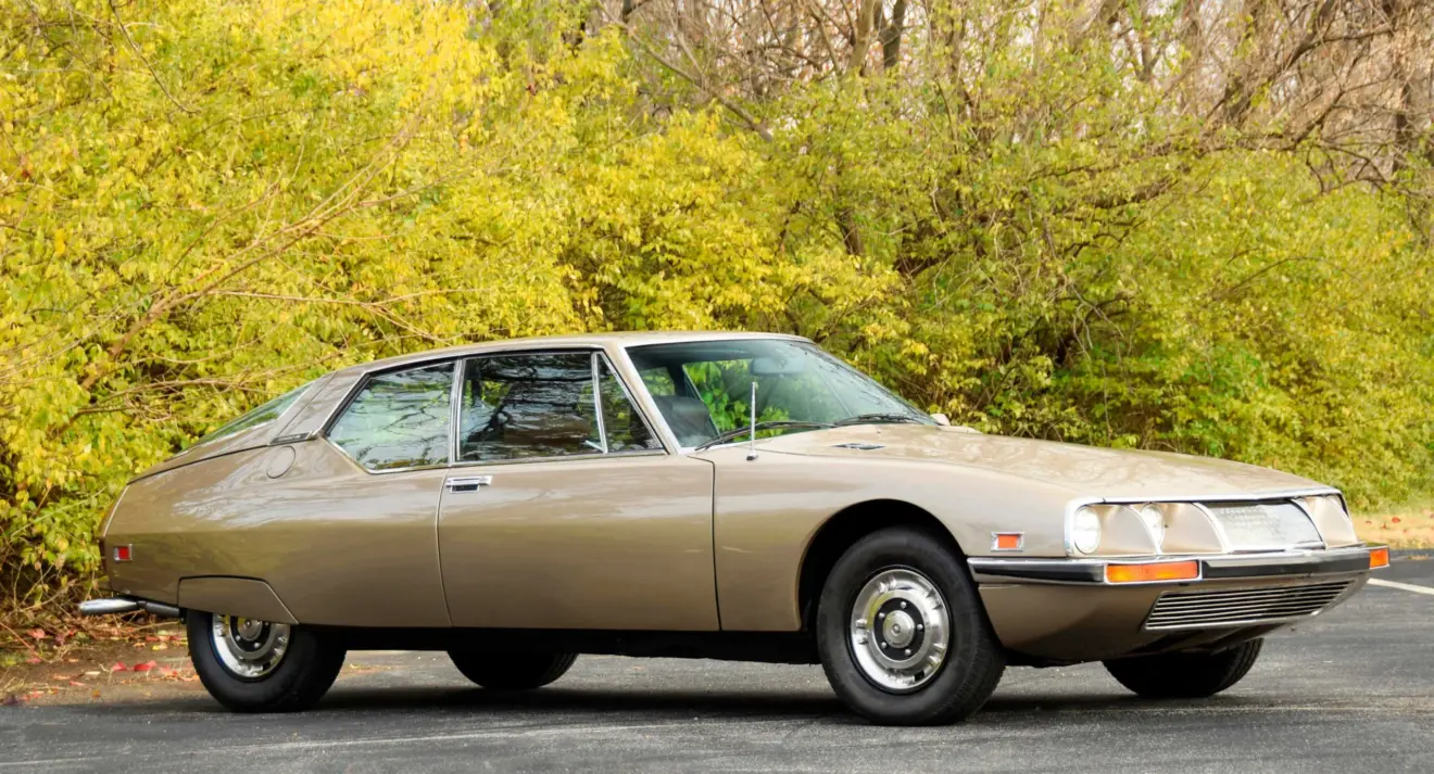 Citroën SM dourado parado de lateral com árvores ao fundo