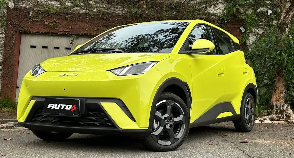 BYD Dolphin Mini amarelo parado em frente a um portão branco e com árvores ao fundo