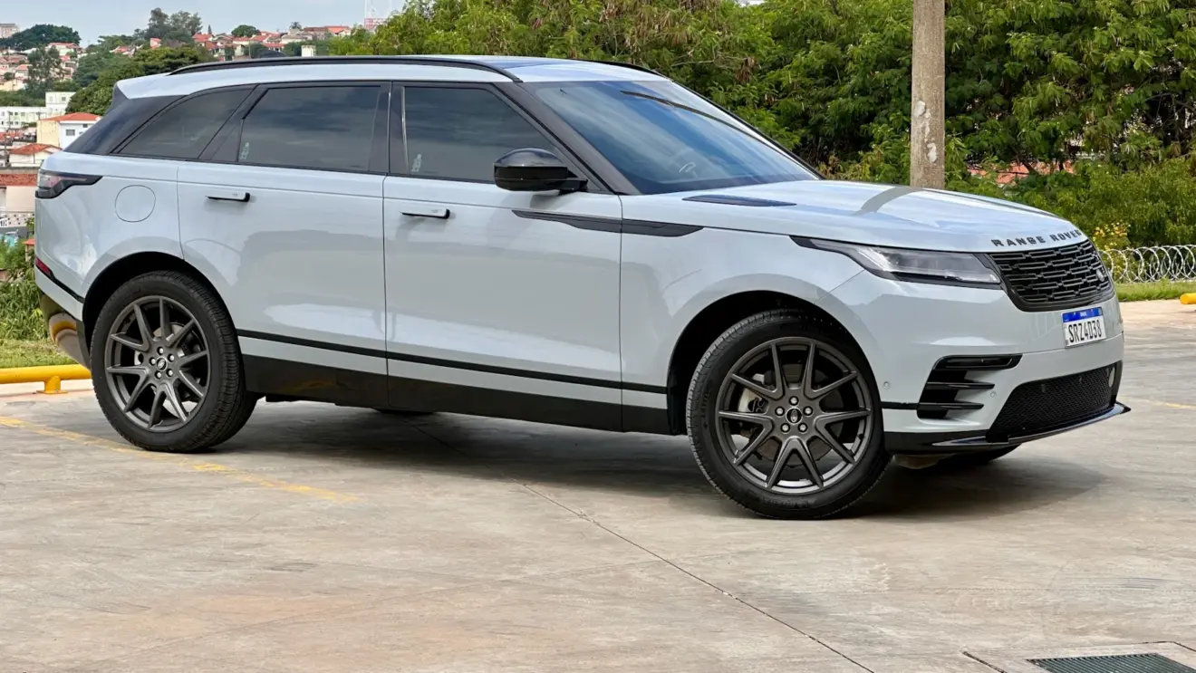 A JLR sofreu um ataque cibernético. E o Land Rover Range Rover Velar prata está parado de lado com uma cidade ao fundo