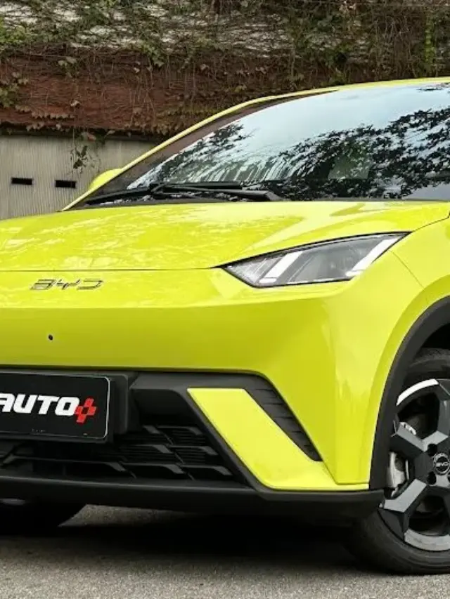 BYD Dolphin Mini amarelo parado em frente a um portão branco e com árvores ao fundo