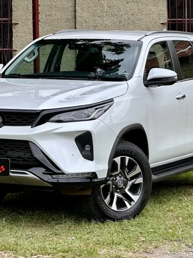 Toyota SW4 SRX Platinum 7 lugares branco de frente com uma casa antiga e um gramado ao fundo