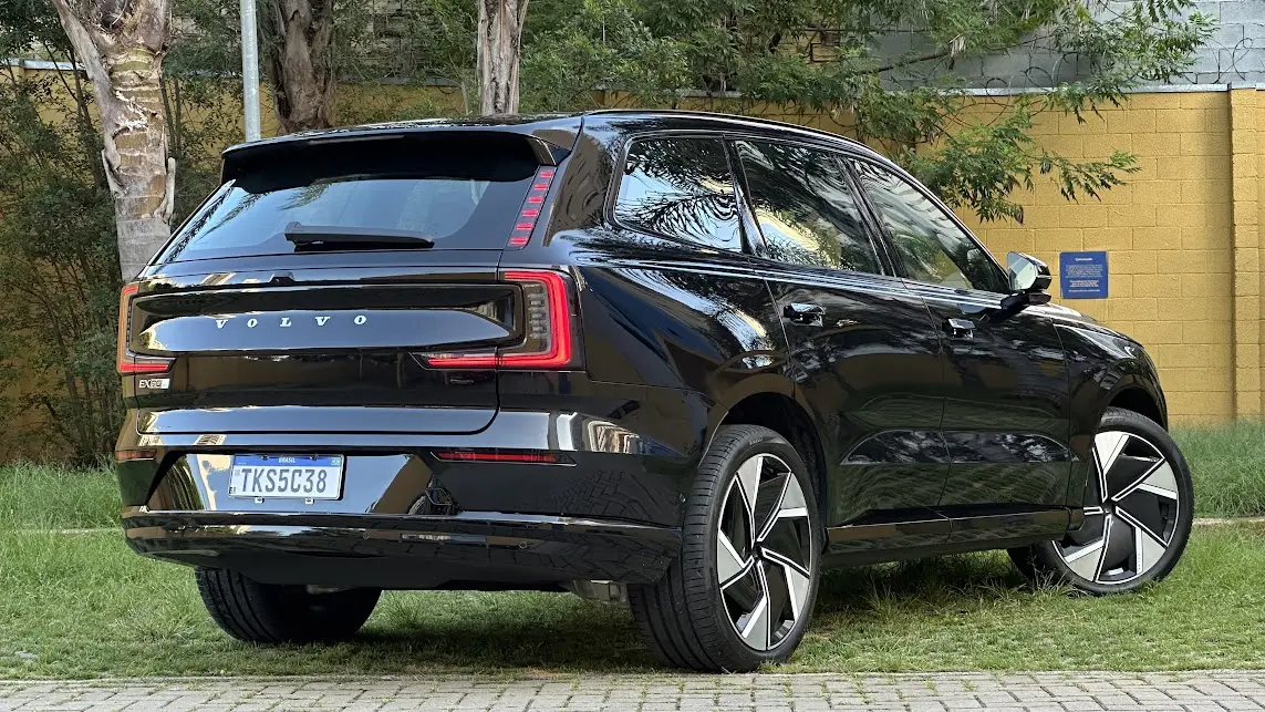 Volvo EX90 Ultra preto parado de traseira com muro amarelo e árvores ao fundo