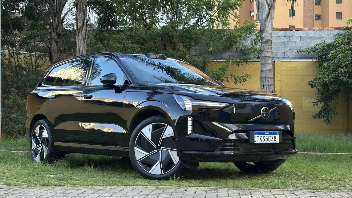 Volvo EX90 Ultra preto parado de frente com muro amarelo e árvores ao fundo