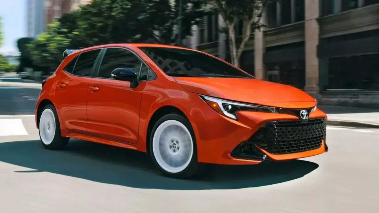 Toyota Corolla hatch FX Edition 2026 laranja com detalhes pretos, visto de lado e com faróis acesos