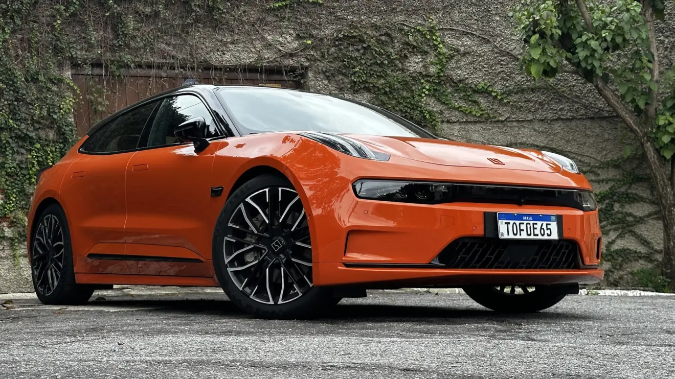 Zeekr 001 laranja parado de frente com muro e plantas ao fundo