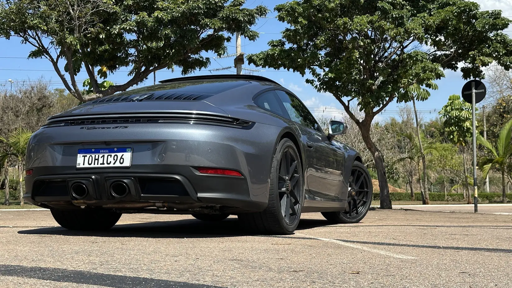 Porsche 911 Carrera GTS cinza parado de traseira com árvores ao fundo
