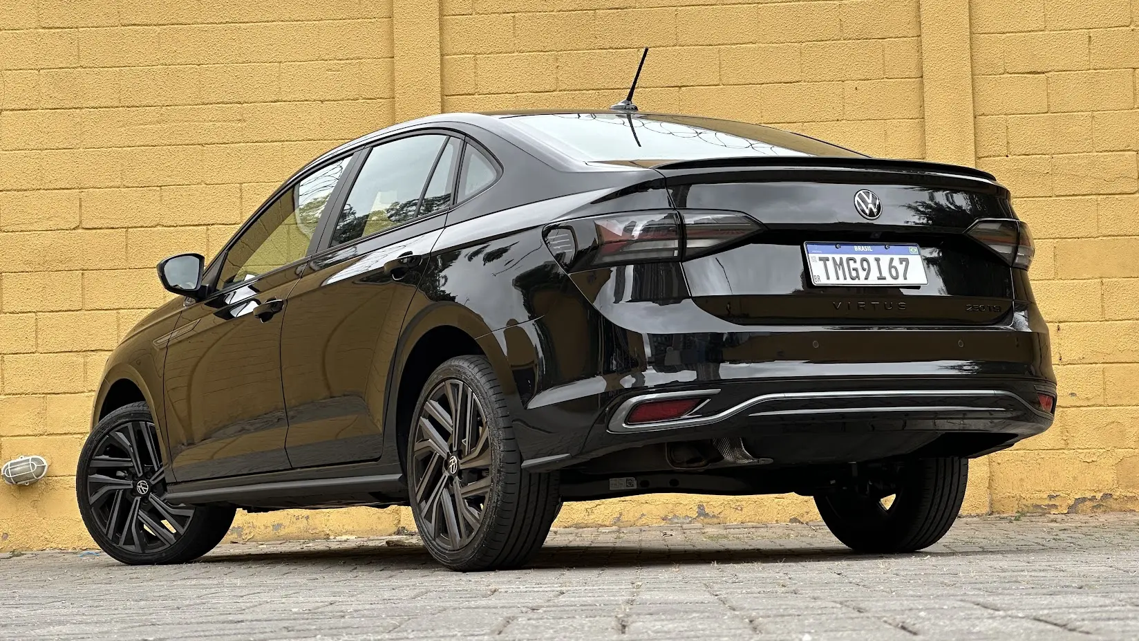 Volkswagen Virtus Exclusive 250 TSI preto parado de traseira com muro amarelo ao fundo