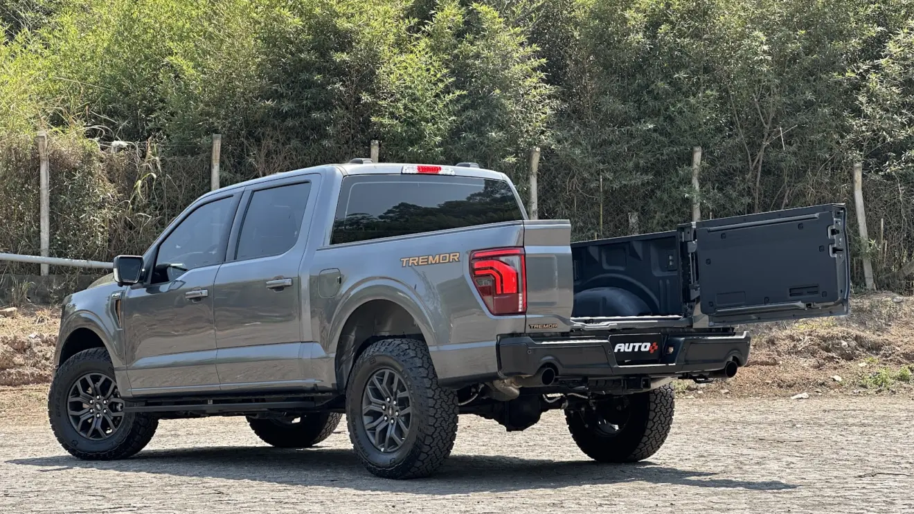 Ford F-150 Tremor cinza parada de traseira com a porção central da tampa da caçamba aberta e árvores ao fundo