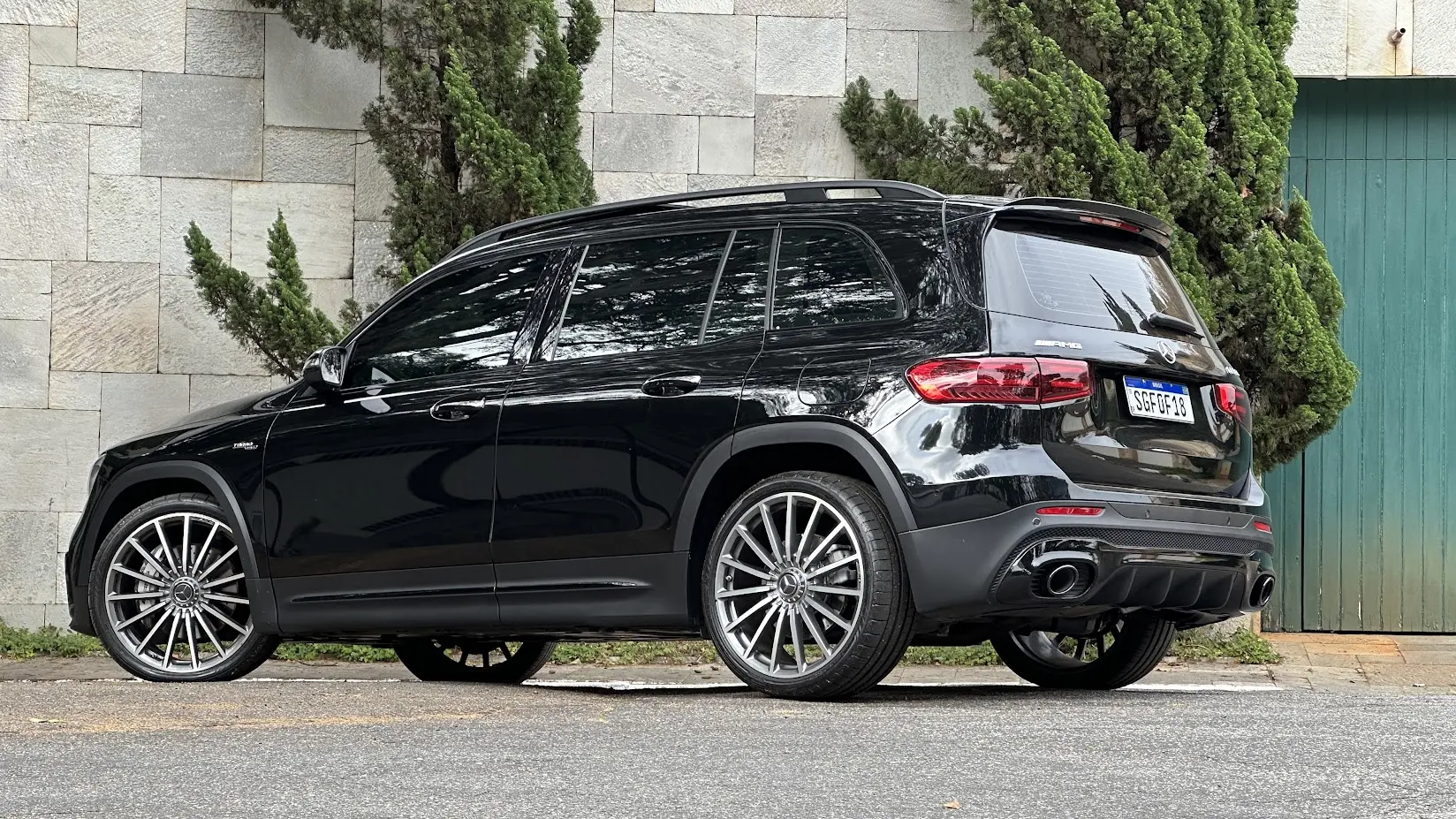 Mercedes-AMG GLB 35 4Matic preto parado de 3x4 traseiro com muro de pedras e árvores ao fundo