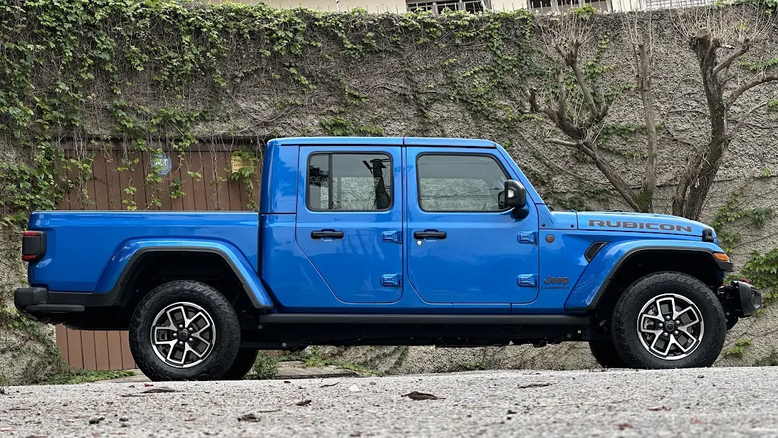 Jeep Gladiator Rubicon azul parado de lateral com muro ao fundo