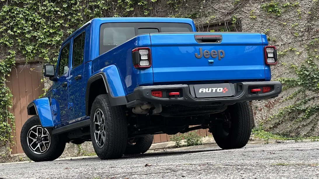 Jeep Gladiator Rubicon azul parado de traseira com muro ao fundo