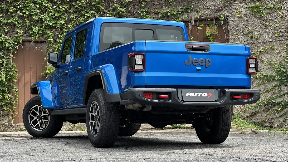 Jeep Gladiator Rubicon azul parado de traseira com muro ao fundo