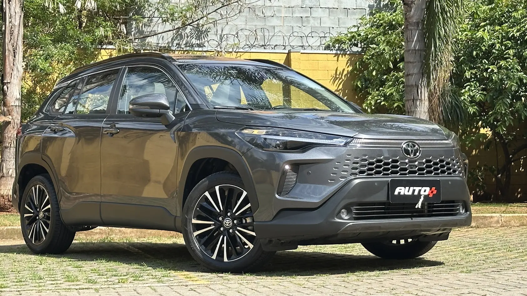 Utilitário esportivo Toyota Corolla Cross XRX cinza parado de frente com muro amarelo e árvores ao fundo