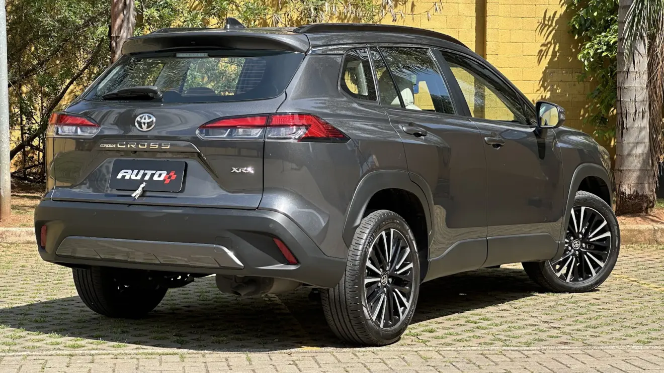 Utilitário esportivo Toyota Corolla Cross XRX cinza parado de traseira com muro amarelo e árvores ao fundo