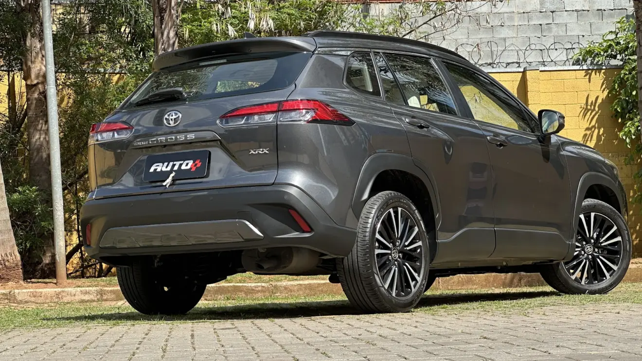 Utilitário esportivo Toyota Corolla Cross cinza parado de traseira com muro amarelo e plantas ao fundo