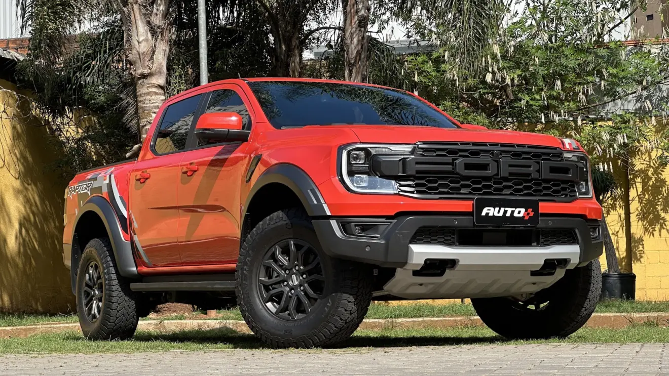 Caminhonete Ford Ranger Raptor laranja parada de dianteira com árvores ao fundo 
