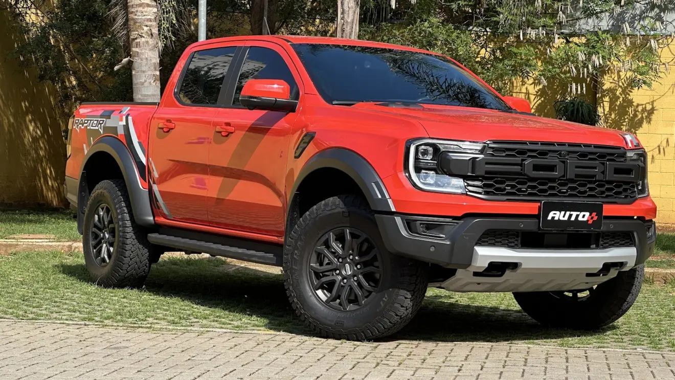 Ford Ranger Raptor laranja parada de frente com muro amarelo e plantas ao fundo
