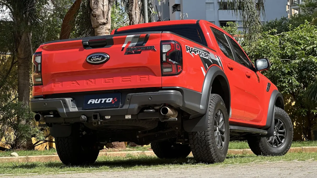 Ford Ranger Raptor laranja parada de traseira com muro amarelo e plantas ao fundo