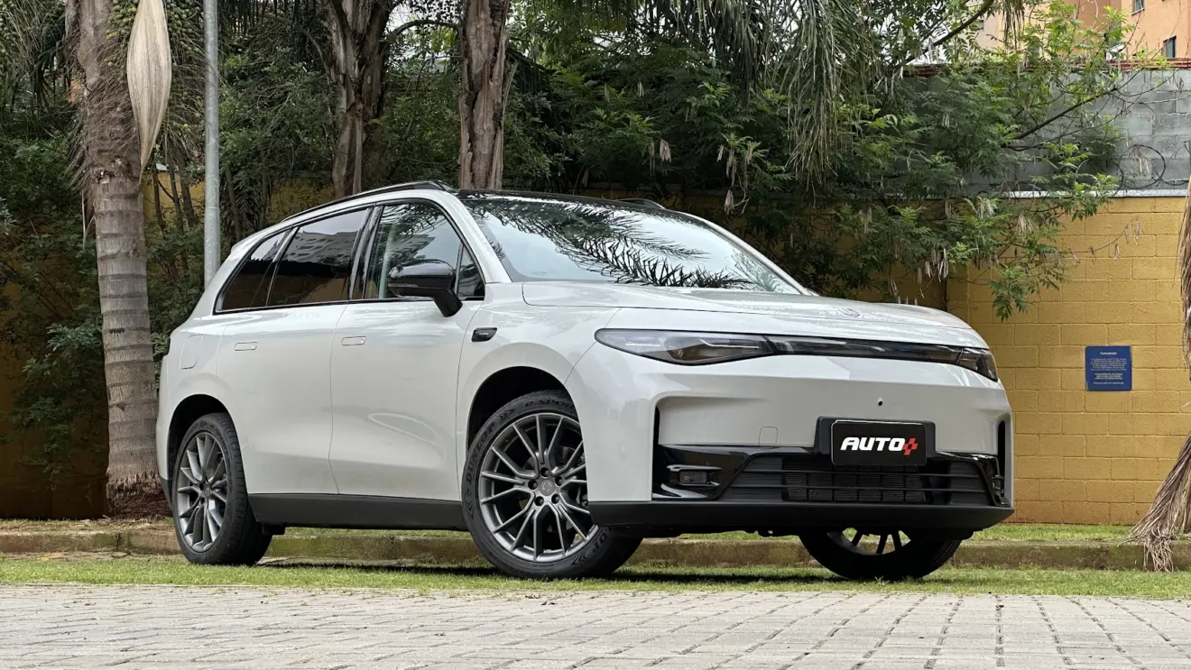 SUV Leapmotor C10 REEV branco parado de dianteira com muro amarelo e plantas ao fundo