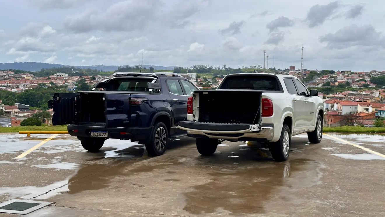 Fiat Toro Ranch azul na chuva de frente ao lado de uma Ram Rampage Big Horn branca ambas com a caçamba aberta