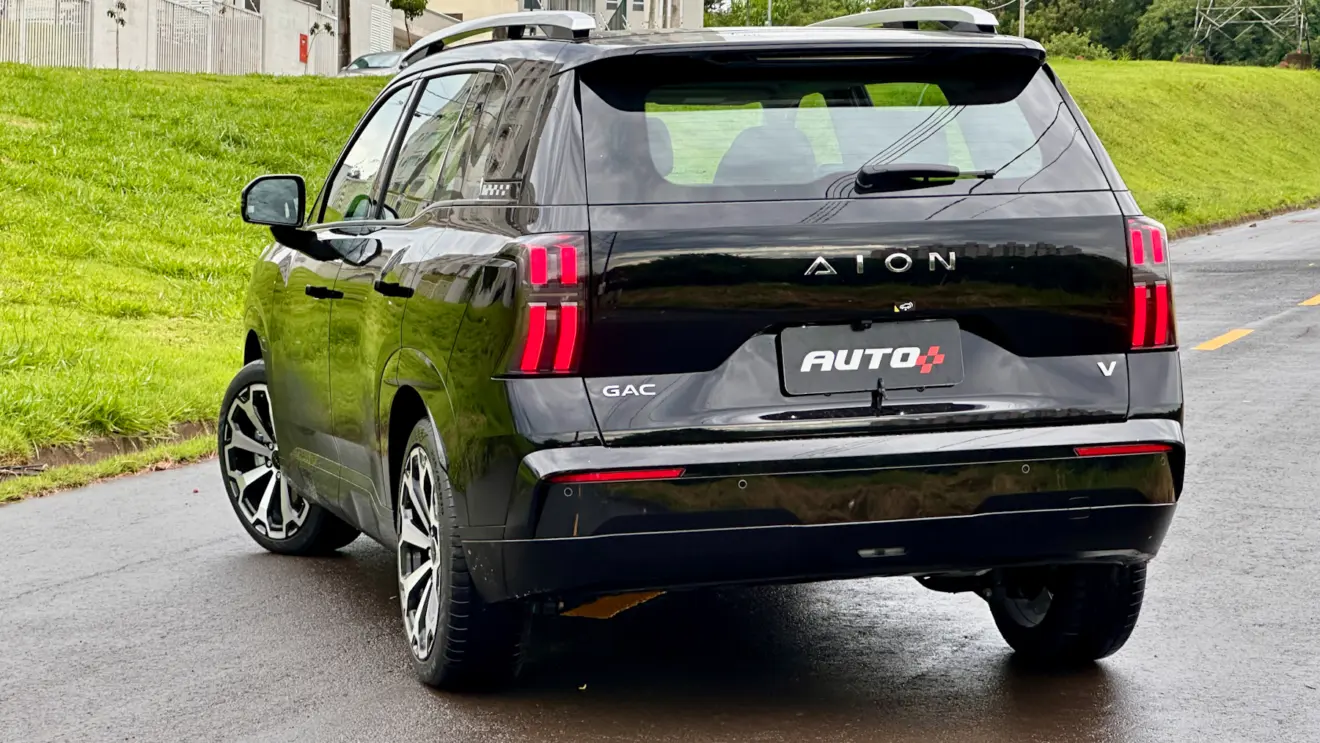 GAC Aion V preto de traseira em uma rua com asfalto molhado e muita grama