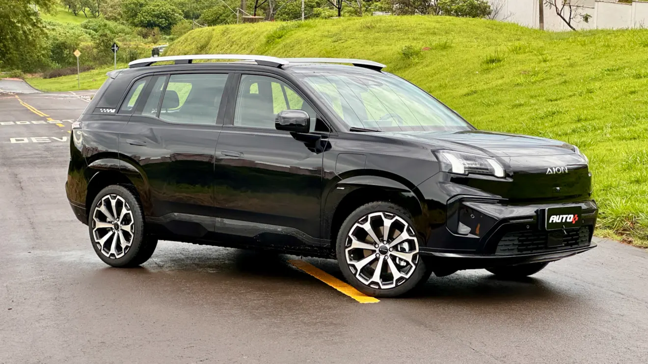 GAC Aion V preto de frente em uma rua com asfalto molhado e muita grama