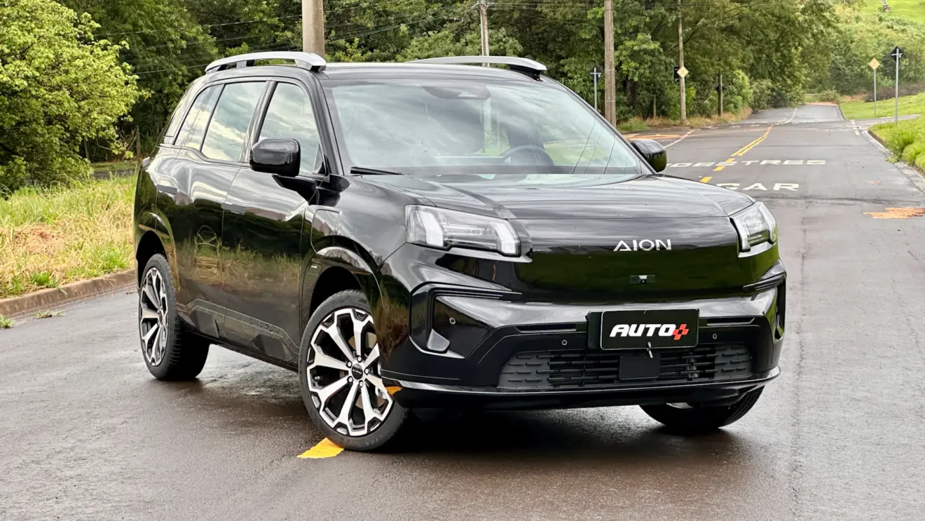 GAC Aion V preto de frente em uma rua com asfalto molhado e muita grama