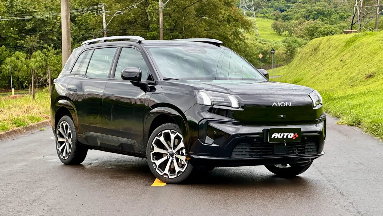 GAC Aion V preto de frente em uma rua com asfalto molhado e muita grama