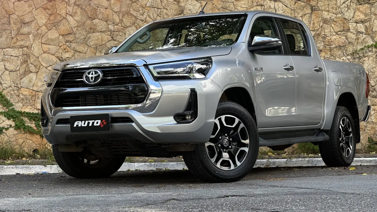 Caminhonete  Toyota Hilux SRV AT prata de frente com muro de pedra ao fundo