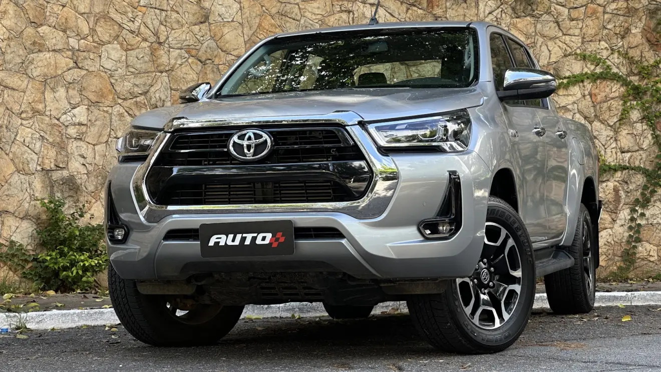 Toyota Hilux SRV prata estacionada de dianteira com muro de pedras ao fundo