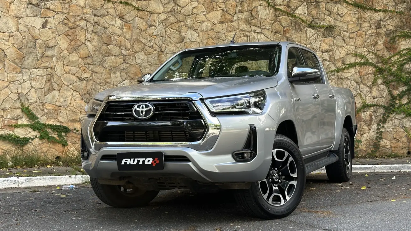 Caminhonete Toyota Hilux SRV AT prata estacionada de frente com muro de pedras ao fundo