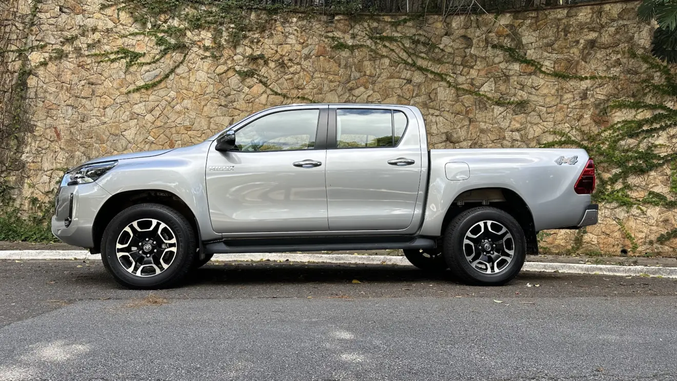 Avaliação da caminhonete Toyota Hilux SRV prata estacionada de lado com muro de pedras ao fundo