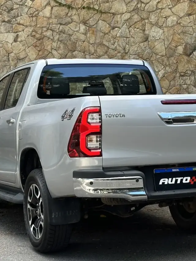 Toyota Hilux SRV prata estacionada de traseira com muro de pedras ao fundo