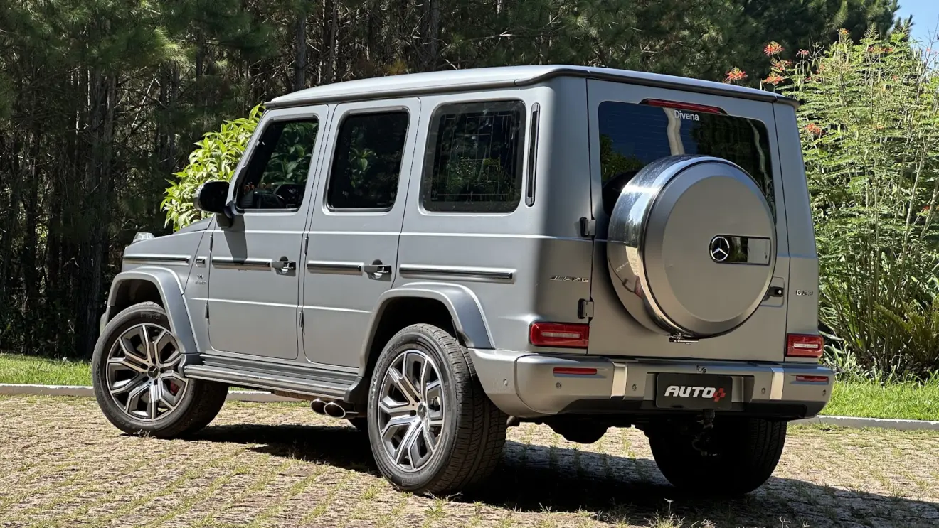 Mercedes-AMG G 63 cinza parado de frente-lateral com árvores ao fundo
