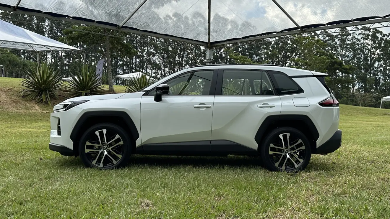 Toyota RAV4 branco parado de lateral na grama e com árvores de fundo