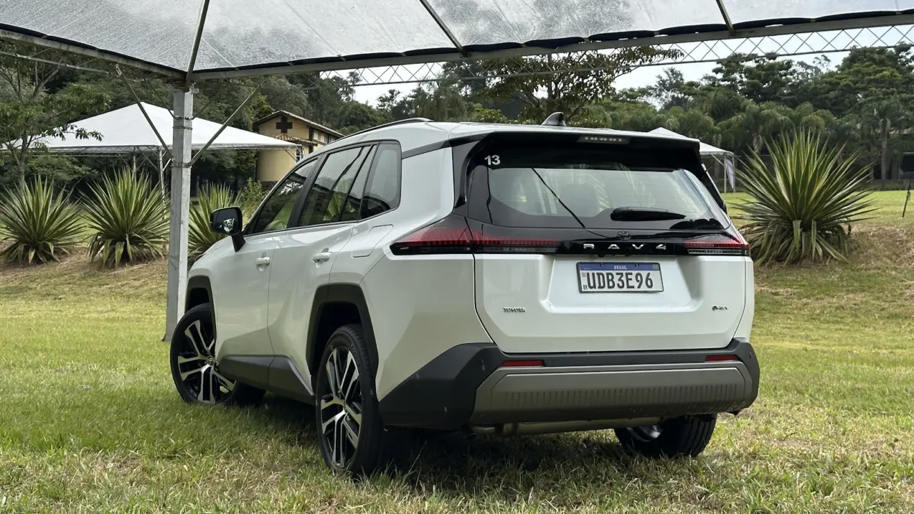 Toyota RAV4 branco parado de traseira na grama e com árvores de fundo
