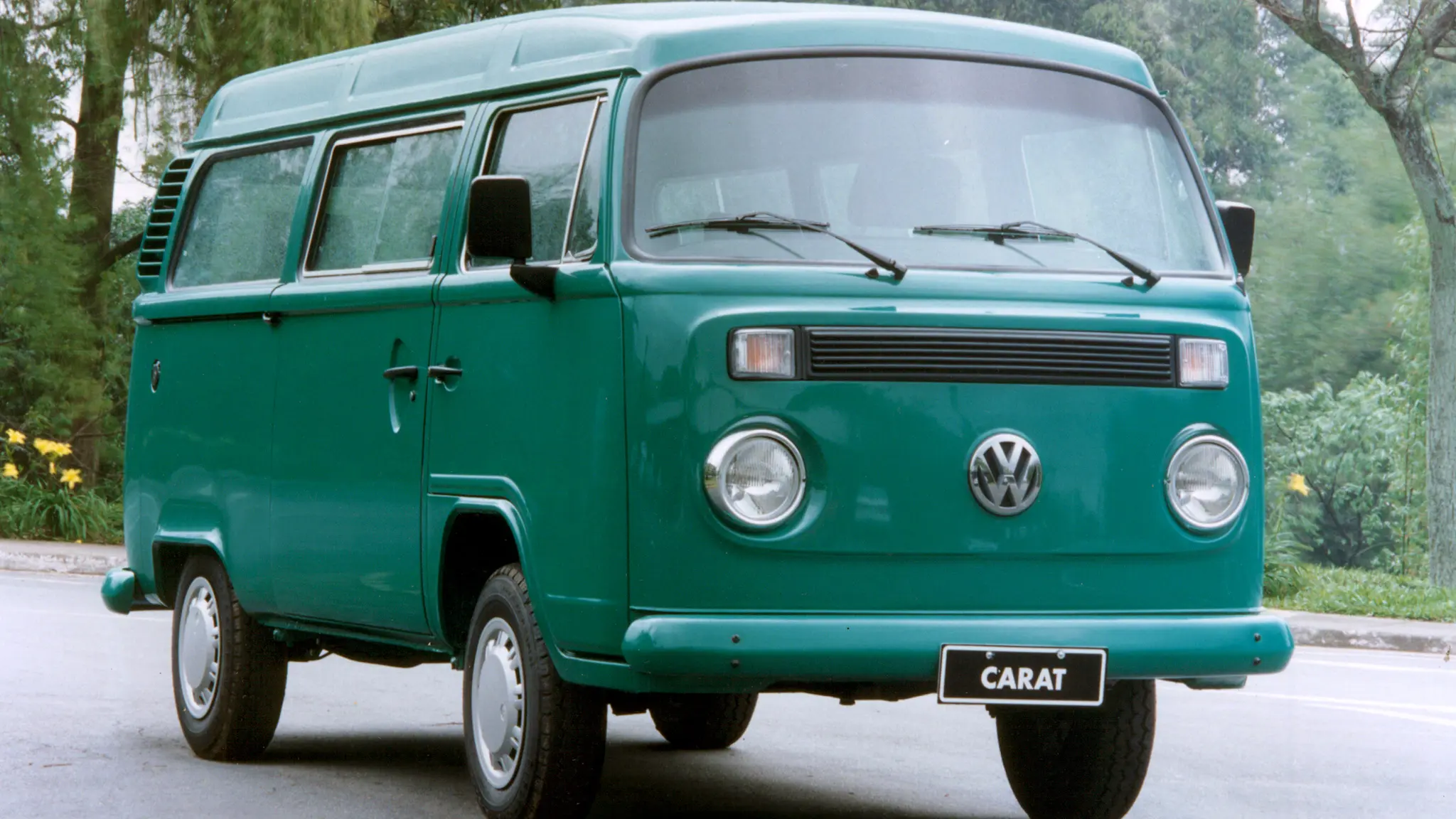 Volkswagen Kombi verde parada de frente com árvores ao fundo