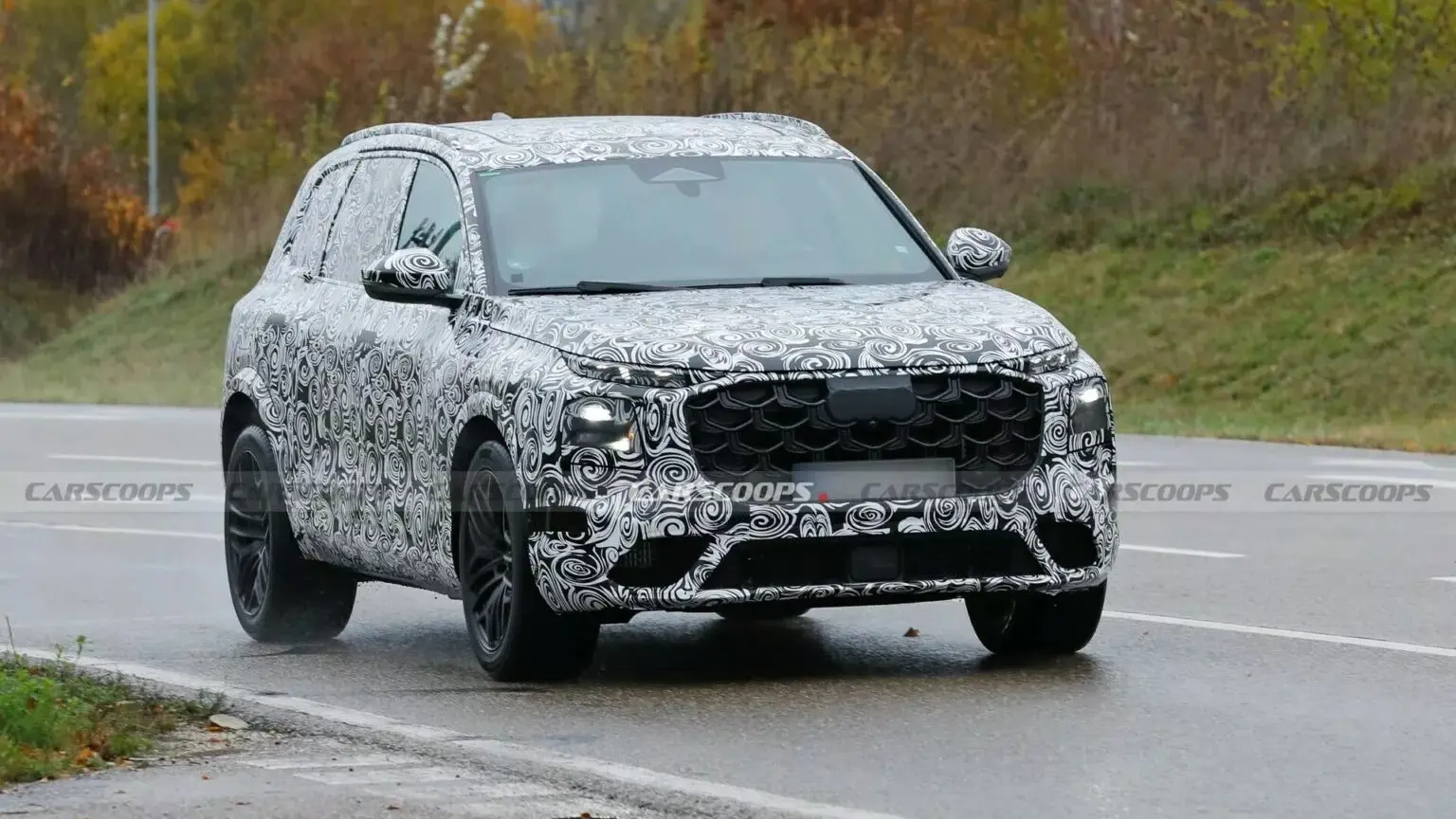 Protótipo do novo Audi SQ7, visto de frente, com camuflagem preta e branca e árvores atrás