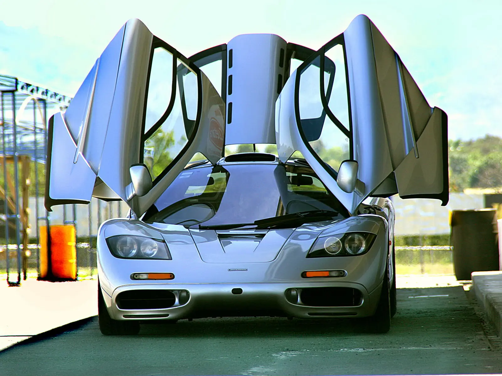 McLaren F1prata parado de frente com as portas abertas verticalmente usa uma tecnologia vinda dos aviões de caça