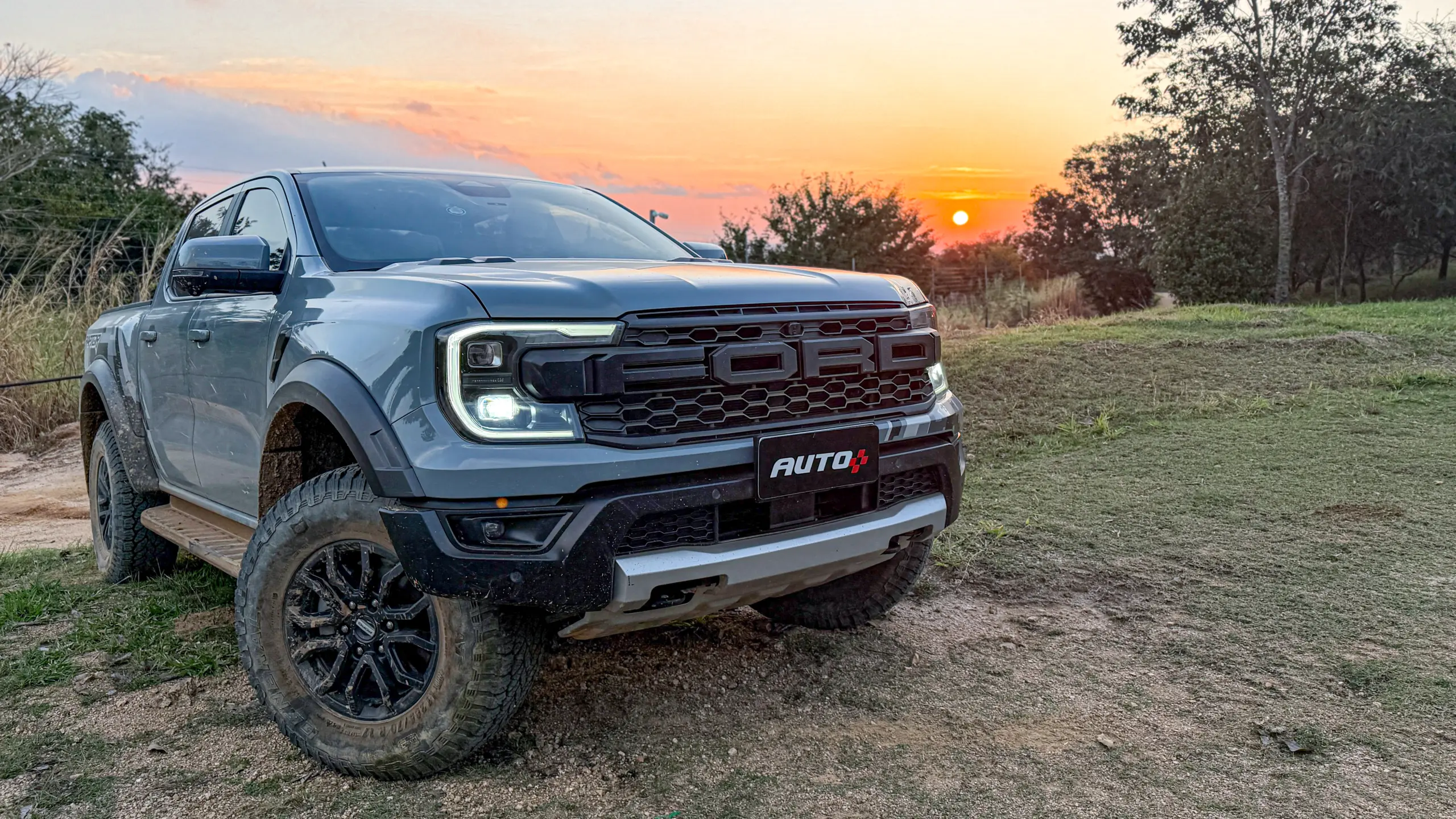 Ford Ranger Raptor suja de barro e terra estática na grama na cor Cinza Interlagos com pôr do sol