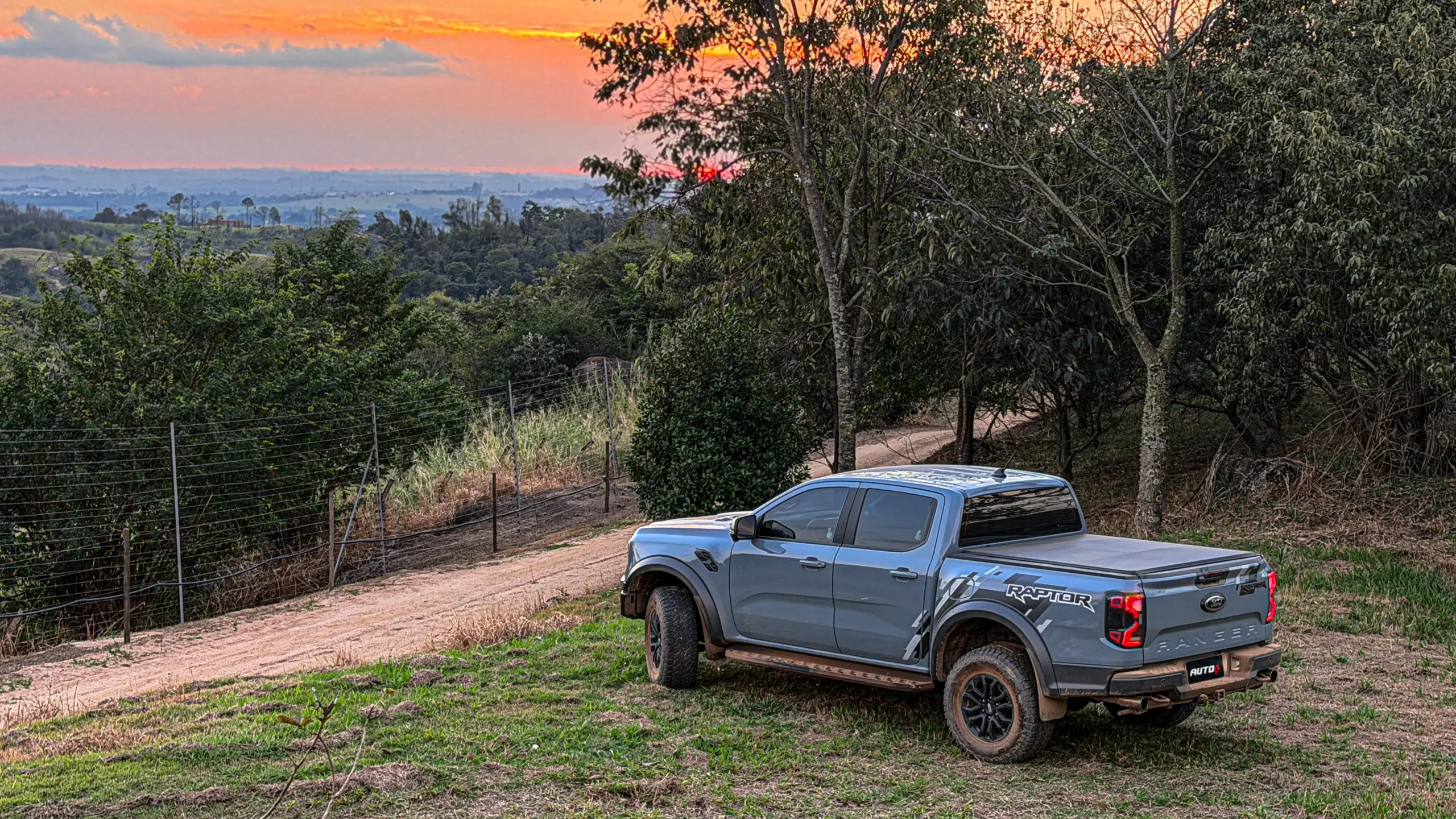 Ford Ranger Raptor suja de barro e terra estática na grama na cor Cinza Interlagos com pôr do sol